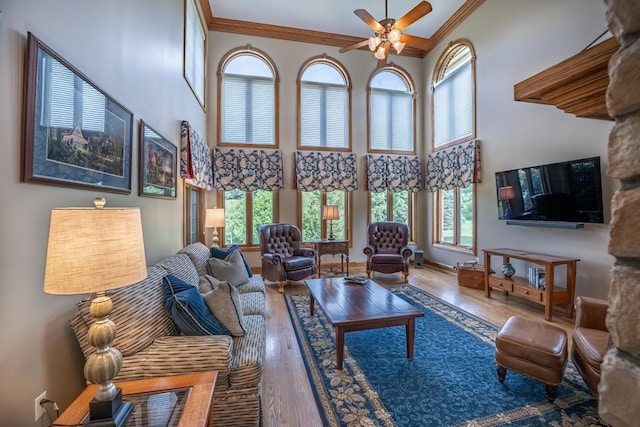 living room featuring crown molding, a towering ceiling, hardwood / wood-style floors, and ceiling fan