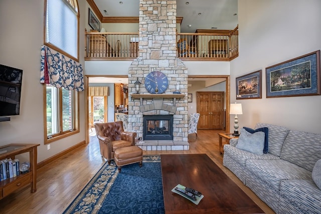 living room with a high ceiling, a stone fireplace, and light hardwood / wood-style flooring