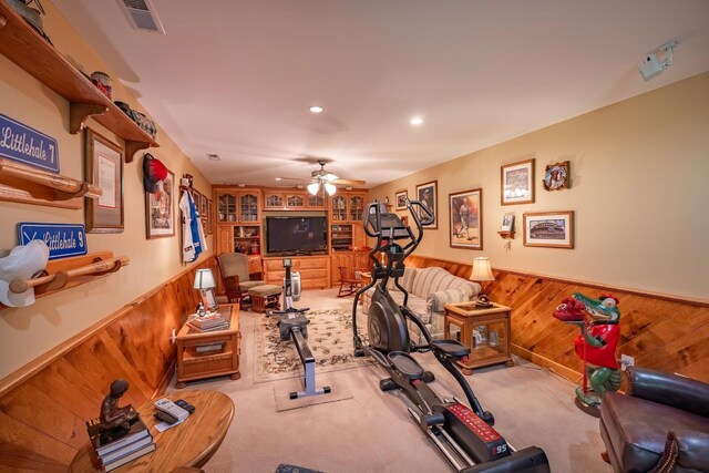 exercise area with light carpet, built in shelves, ceiling fan, and wood walls