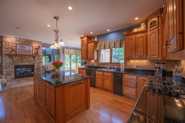 kitchen featuring a stone fireplace, dishwasher, hanging light fixtures, a center island, and light hardwood / wood-style floors