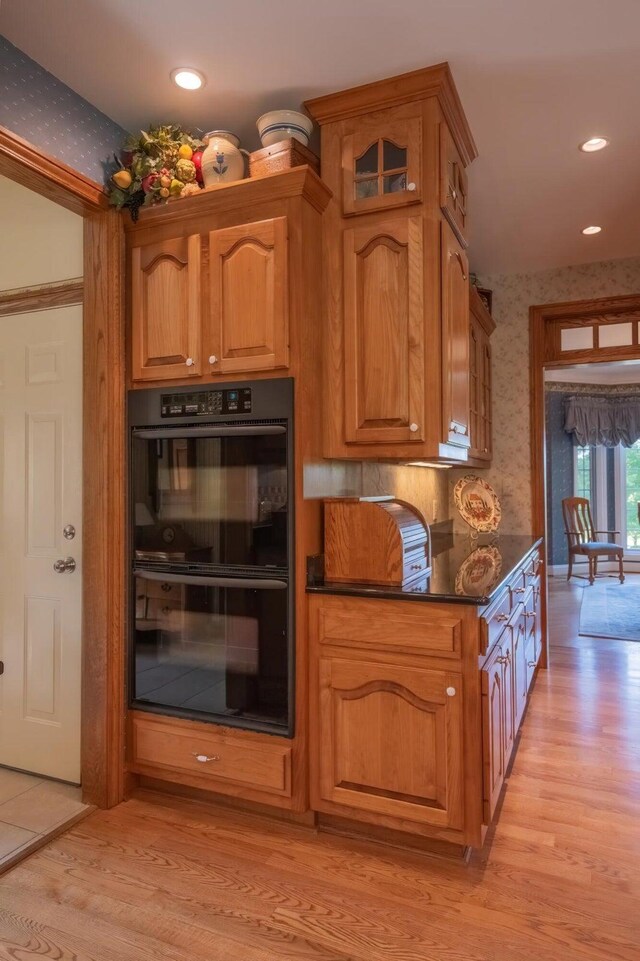 kitchen with double oven, dark stone counters, and light wood-type flooring