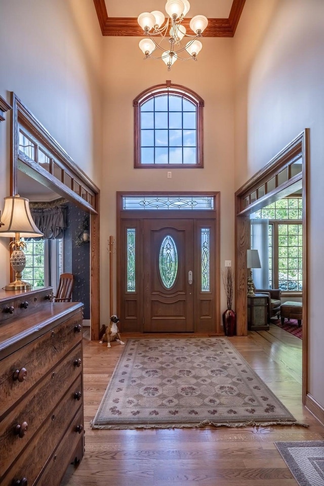 foyer entrance with light hardwood / wood-style flooring, ornamental molding, a chandelier, and plenty of natural light