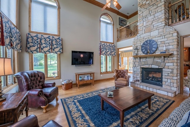 living room featuring a stone fireplace, a towering ceiling, wood-type flooring, ornamental molding, and ceiling fan