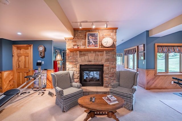 carpeted living room featuring track lighting, a stone fireplace, and wood walls