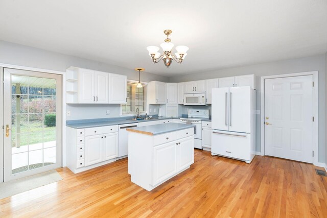 kitchen with white appliances, white cabinetry, hanging light fixtures, a kitchen island, and light wood-type flooring