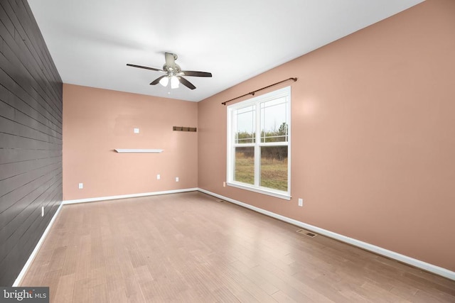 spare room with visible vents, a ceiling fan, wood walls, wood finished floors, and baseboards