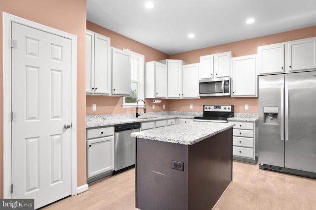 kitchen with light wood finished floors, stainless steel appliances, a sink, a kitchen island, and light stone countertops