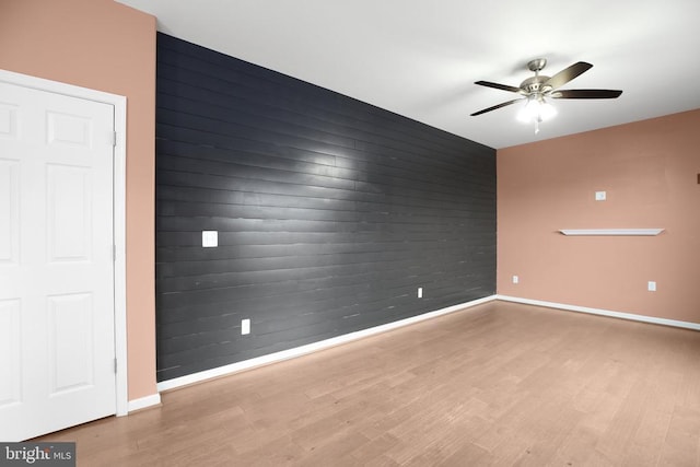 spare room featuring a ceiling fan, an accent wall, baseboards, and wood finished floors