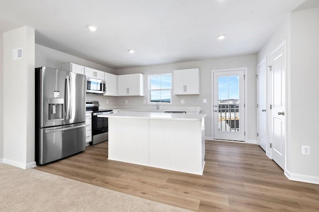 kitchen with a kitchen island, appliances with stainless steel finishes, white cabinets, and light hardwood / wood-style flooring