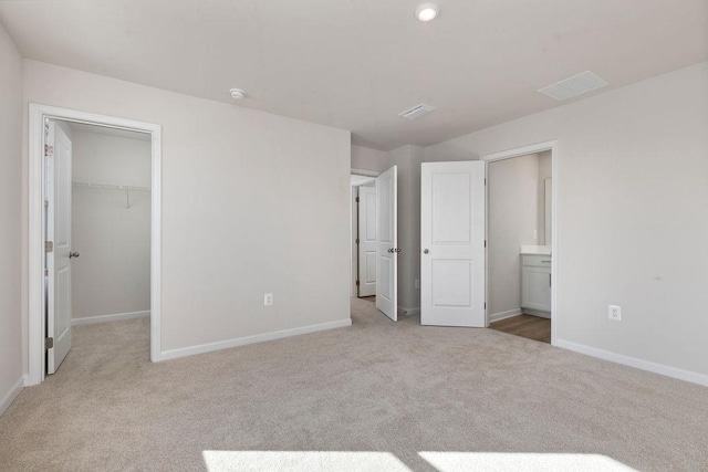 unfurnished bedroom featuring ensuite bathroom, a spacious closet, and light carpet