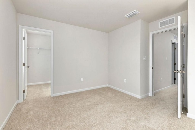 unfurnished bedroom featuring a walk in closet and light carpet