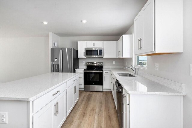 kitchen with sink, light stone counters, light wood-type flooring, appliances with stainless steel finishes, and white cabinets