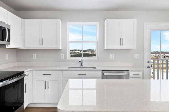 kitchen with sink, white cabinetry, stainless steel appliances, light stone counters, and a healthy amount of sunlight