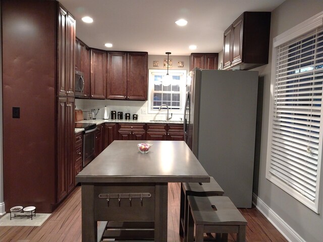 kitchen with appliances with stainless steel finishes, sink, hanging light fixtures, a center island, and light hardwood / wood-style floors