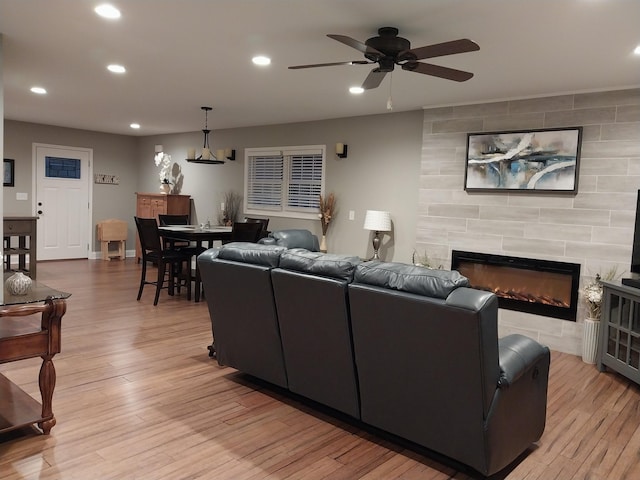 living room with ceiling fan, a tiled fireplace, and light wood-type flooring