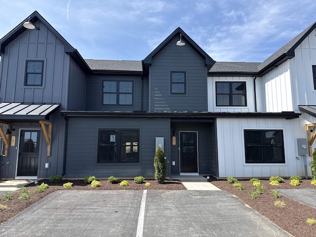 modern inspired farmhouse with board and batten siding, uncovered parking, and roof with shingles