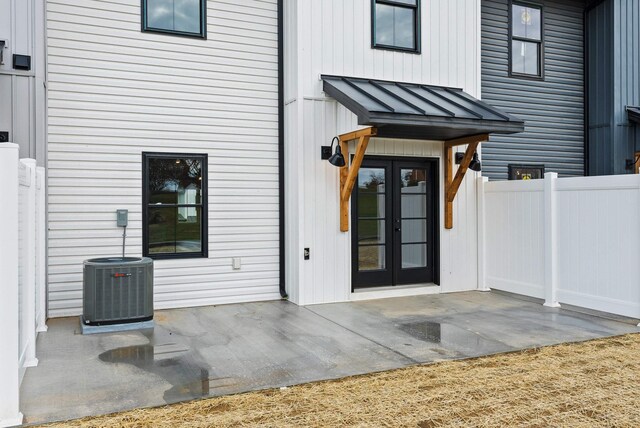 view of exterior entry featuring a standing seam roof, french doors, a patio area, central AC, and fence