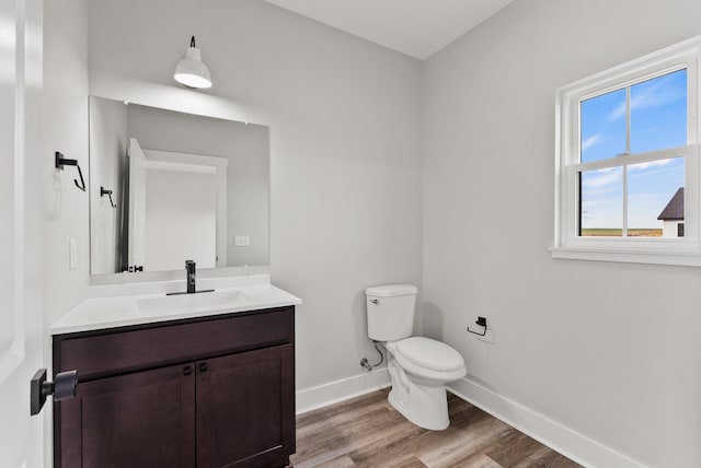 half bath with baseboards, wood finished floors, toilet, and vanity
