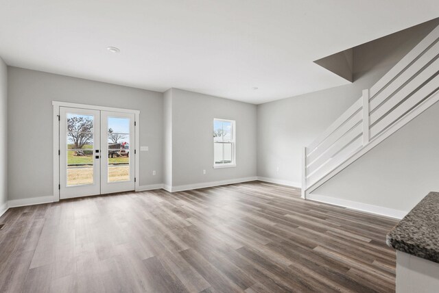 unfurnished living room with baseboards, dark wood-type flooring, and stairway