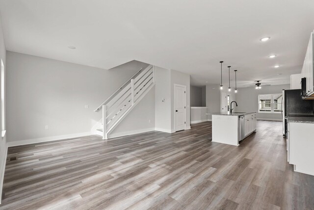 unfurnished living room with ceiling fan, a sink, baseboards, stairway, and light wood-style flooring