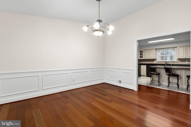 unfurnished dining area with visible vents, a wainscoted wall, an inviting chandelier, and wood finished floors