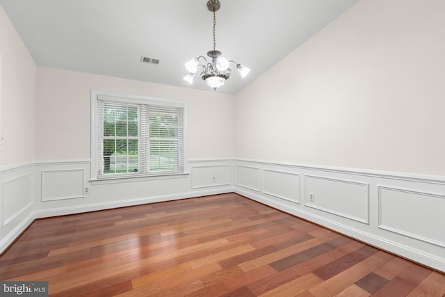 spare room with wood finished floors, a notable chandelier, lofted ceiling, and visible vents