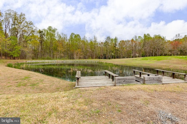 view of dock with a wooded view, a yard, and a water view
