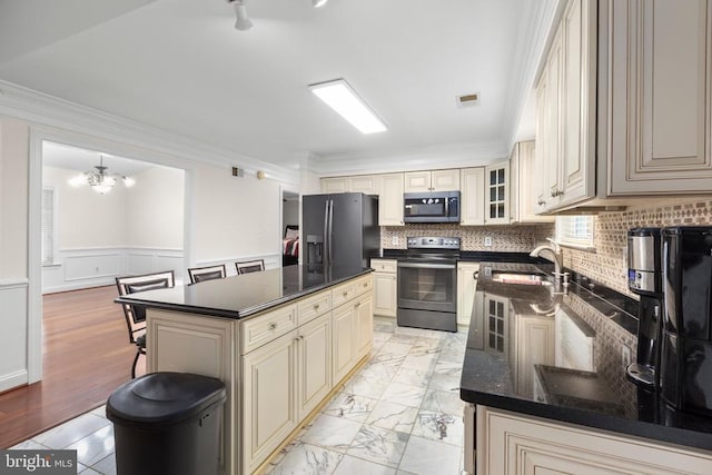 kitchen with a notable chandelier, a sink, ornamental molding, appliances with stainless steel finishes, and cream cabinets