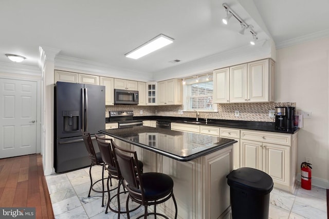 kitchen with rail lighting, cream cabinetry, a kitchen bar, appliances with stainless steel finishes, and a sink
