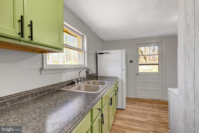 kitchen featuring green cabinetry, freestanding refrigerator, a sink, dark countertops, and light wood-type flooring