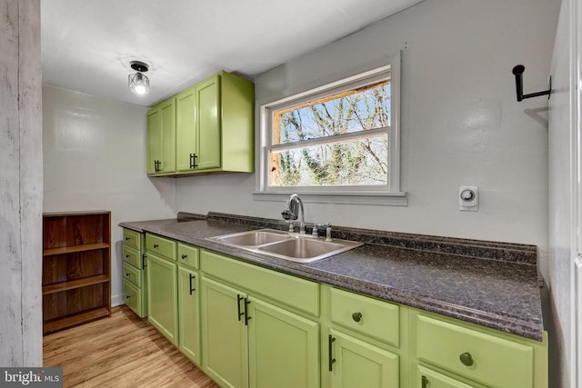 kitchen with a sink, light wood-style flooring, dark countertops, and green cabinets