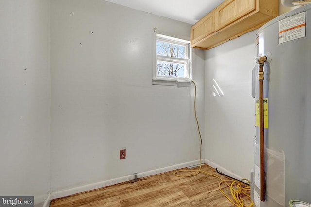 clothes washing area with water heater, light wood-style flooring, and baseboards