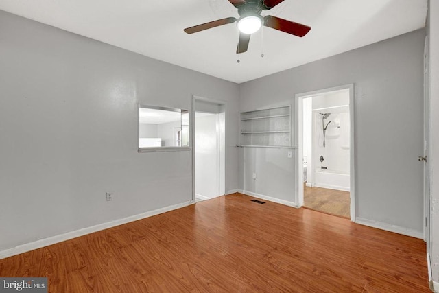 unfurnished bedroom featuring ensuite bath, visible vents, wood finished floors, and baseboards