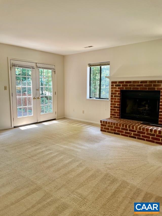 unfurnished living room featuring a fireplace, french doors, and carpet