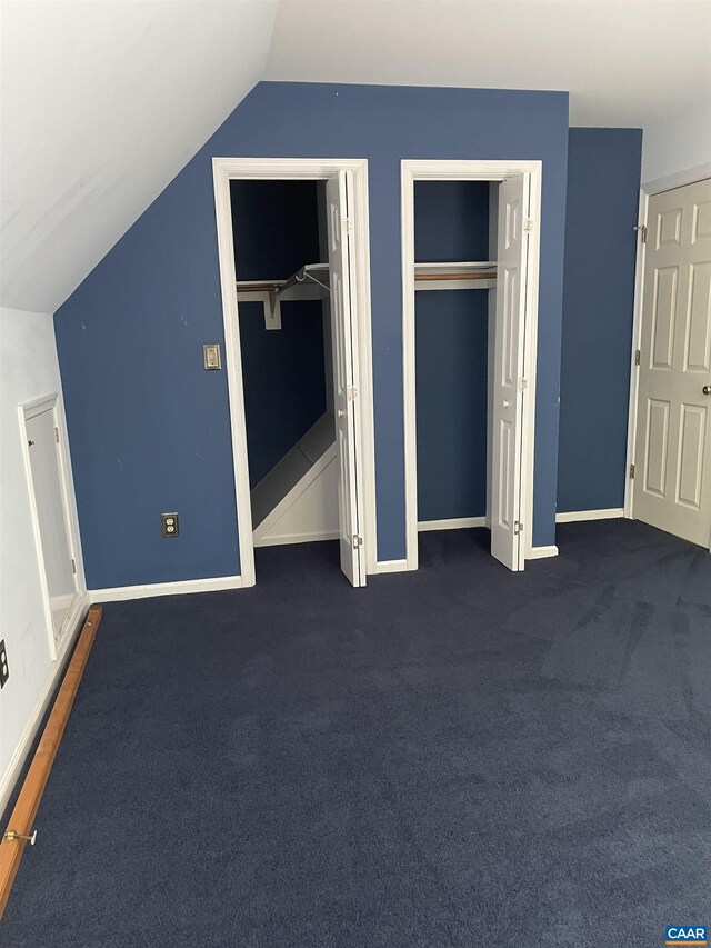 unfurnished bedroom featuring dark colored carpet, lofted ceiling, and two closets