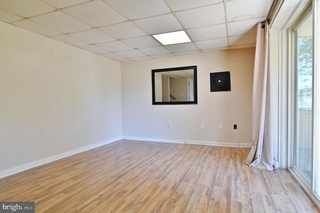empty room featuring baseboards, a wealth of natural light, a paneled ceiling, and light wood-style floors