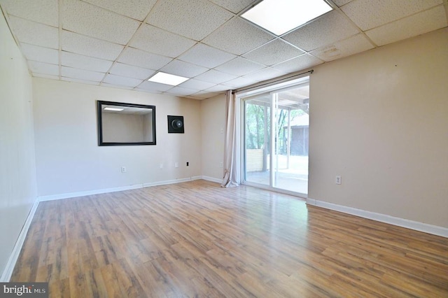 spare room featuring baseboards, a paneled ceiling, and wood finished floors