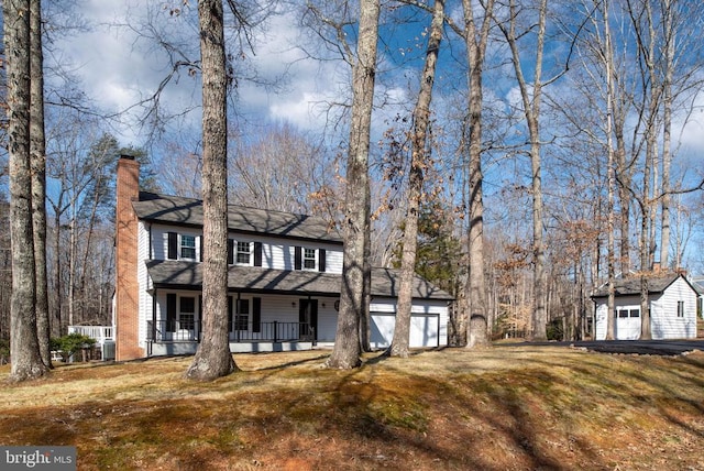 view of front facade featuring a chimney, a porch, an attached garage, an outdoor structure, and a front lawn