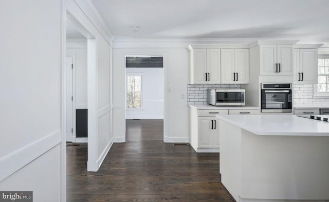 kitchen featuring stainless steel appliances, light countertops, tasteful backsplash, dark wood finished floors, and crown molding