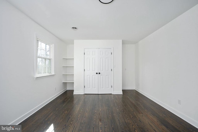 unfurnished bedroom featuring dark wood-type flooring, a closet, and baseboards