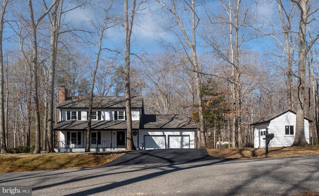 view of front of property with covered porch, aphalt driveway, a chimney, and an attached garage