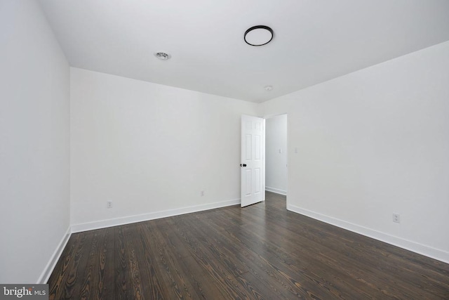 spare room featuring baseboards and dark wood-style flooring