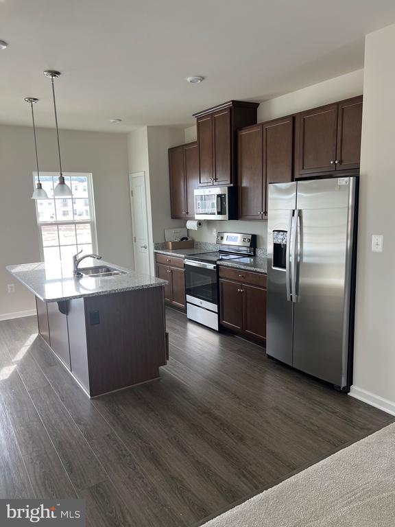 kitchen with appliances with stainless steel finishes, sink, hanging light fixtures, a kitchen island with sink, and dark brown cabinets