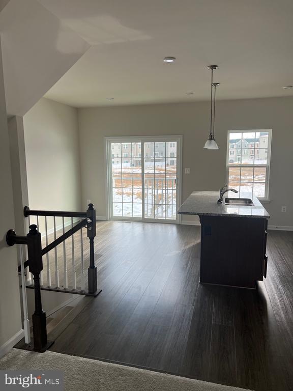 kitchen featuring dark wood-type flooring, sink, light stone counters, hanging light fixtures, and an island with sink