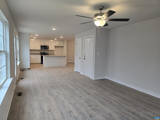 unfurnished living room with a wealth of natural light, ceiling fan, and light wood-type flooring