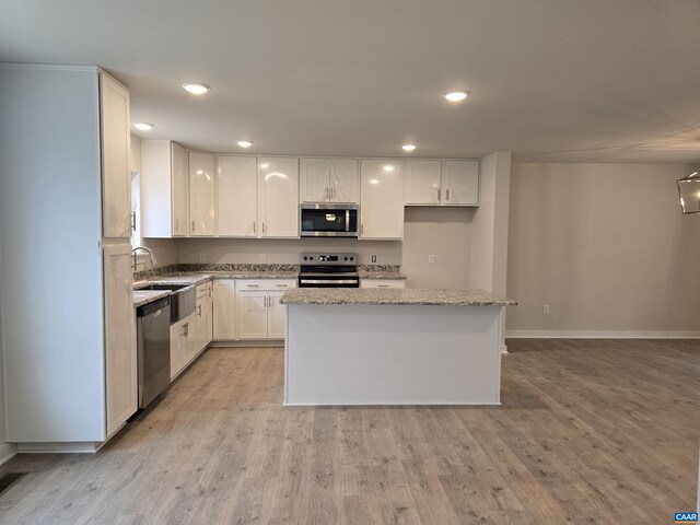 kitchen with light stone counters, appliances with stainless steel finishes, a kitchen island, and white cabinets