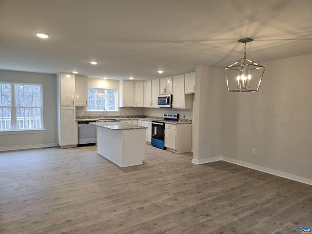 kitchen with pendant lighting, white cabinetry, stainless steel appliances, a center island, and light stone counters