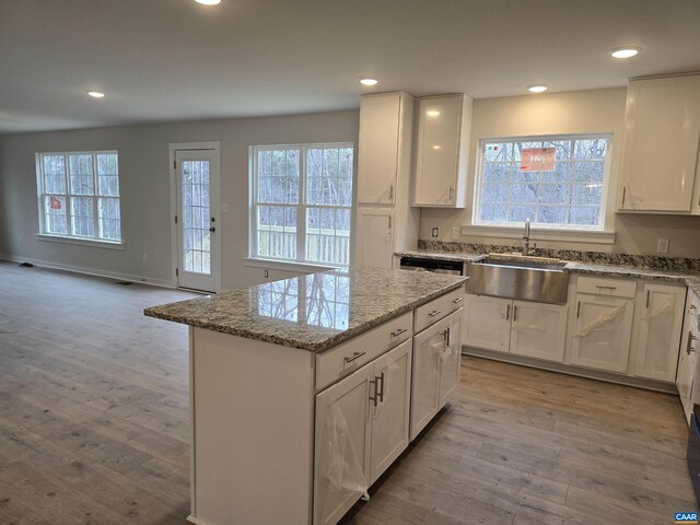 kitchen with white cabinetry, a center island, sink, and light stone counters