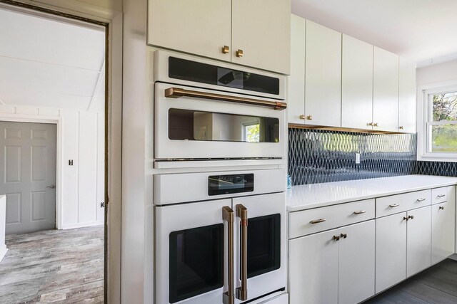 kitchen with light wood-style flooring, light countertops, white cabinets, and double oven