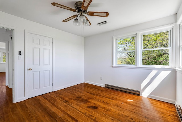 unfurnished bedroom featuring visible vents, a baseboard radiator, multiple windows, and wood finished floors